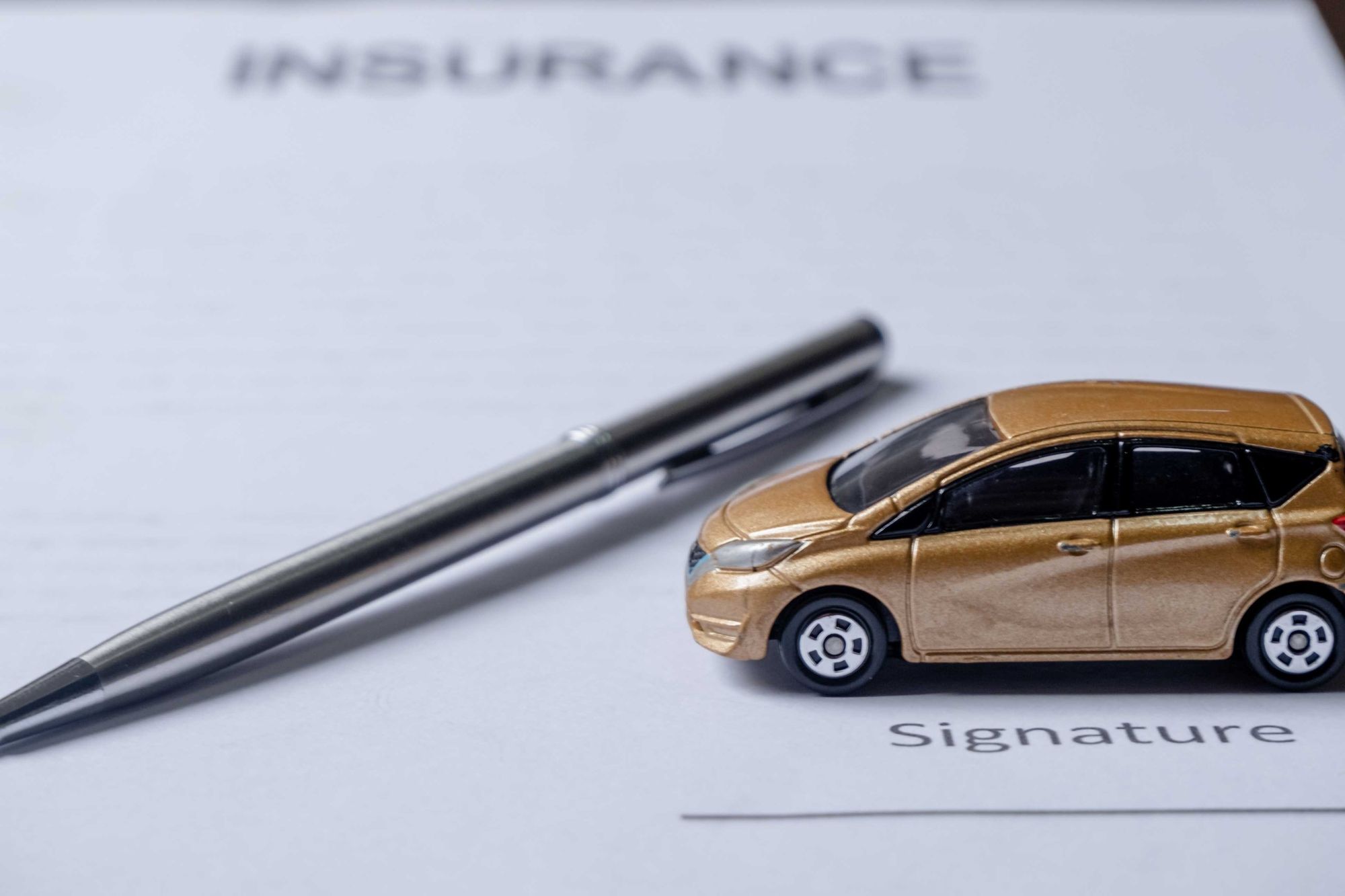 Bolígrafo y coche de juguete encima de los documentos del seguro del coche